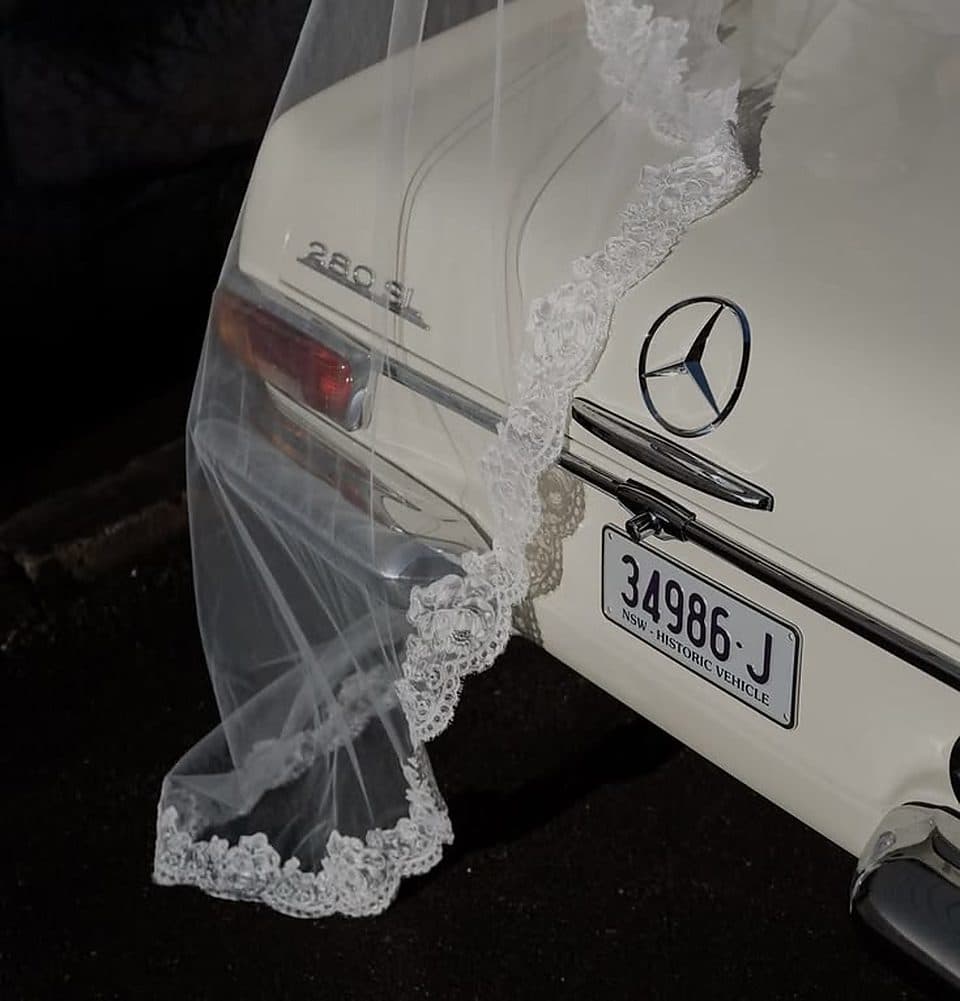 A lace bridal veil draped over a vintage white car